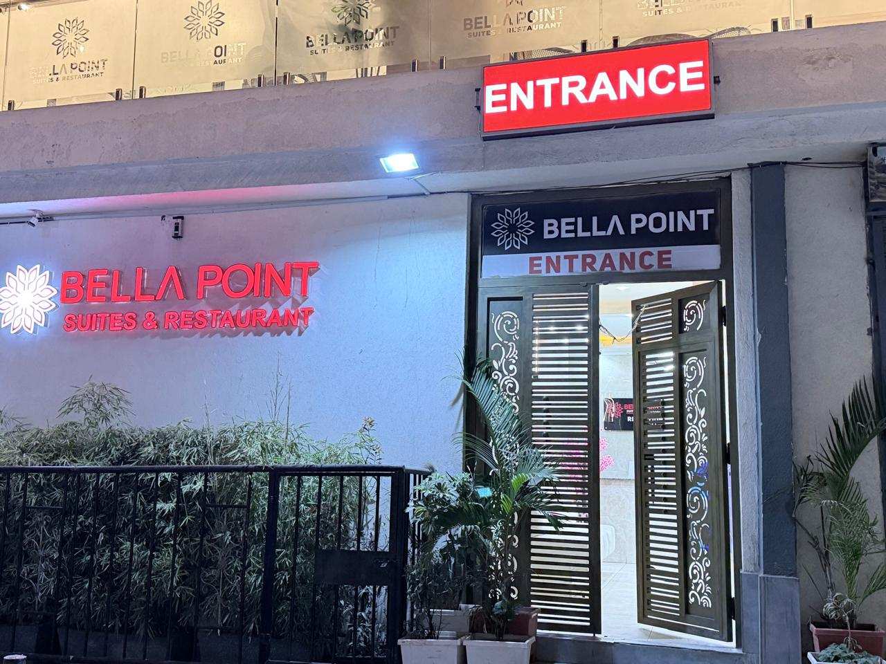 The Bellapoint Suites entrance at night, with the lit red sign, open lattice doors and potted plants.